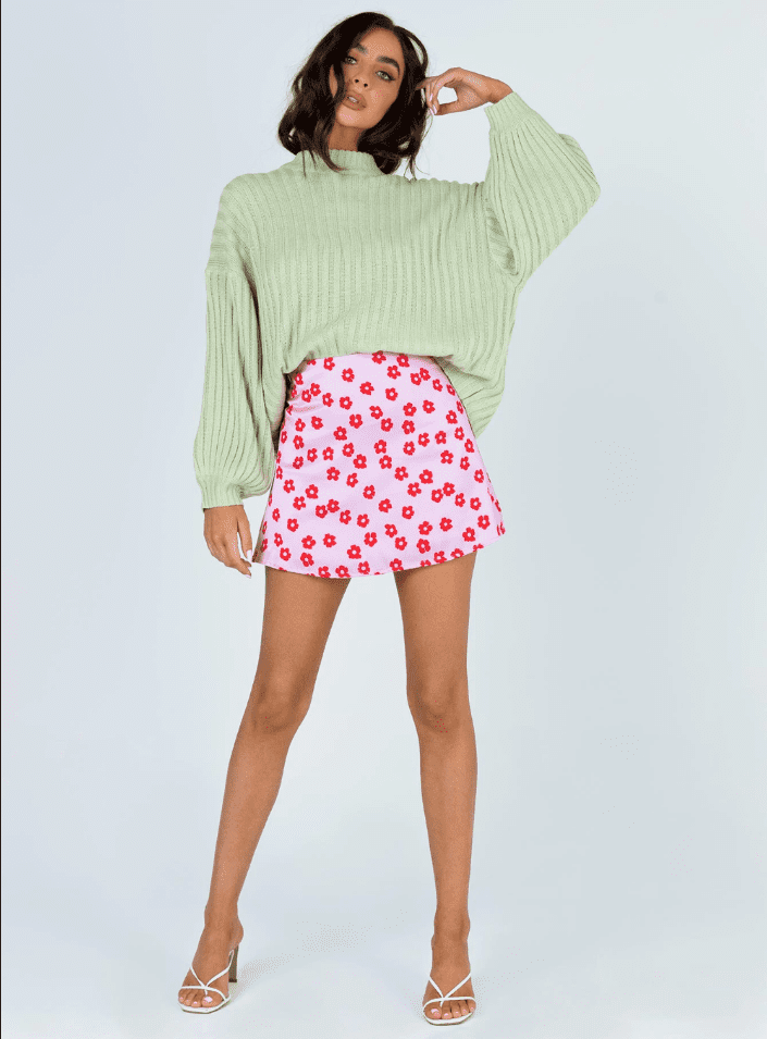 A woman wearing a sage green top and a pink skirt